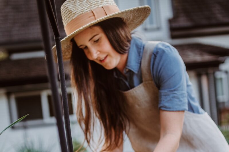 A woman in an apron and hat tending to flowers